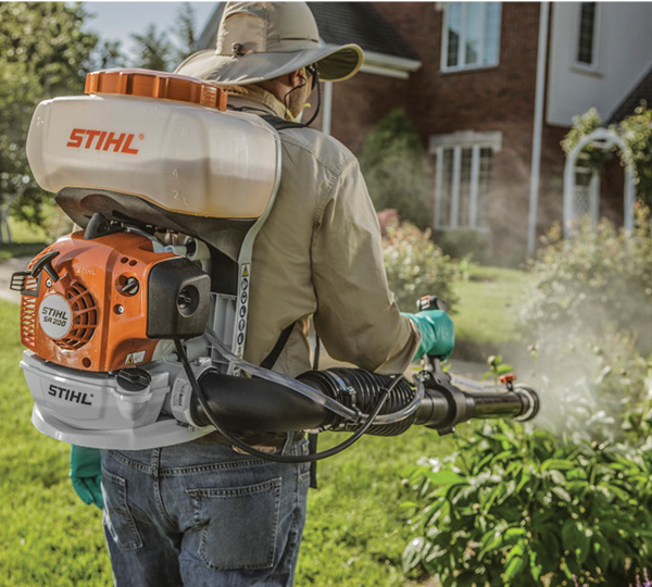 Professional pest control technician on property applying a spray organic mosquito and tick prevention treatment for home, yard, and garden.